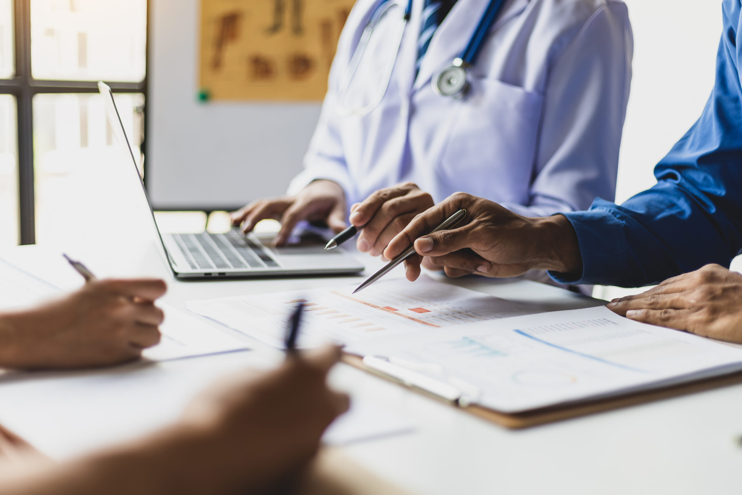 Team, medical analysts and doctors consulting with paperwork of graphs, data and charts in hospital conference room. Healthcare staff discussing statistics, results of research and innovation.